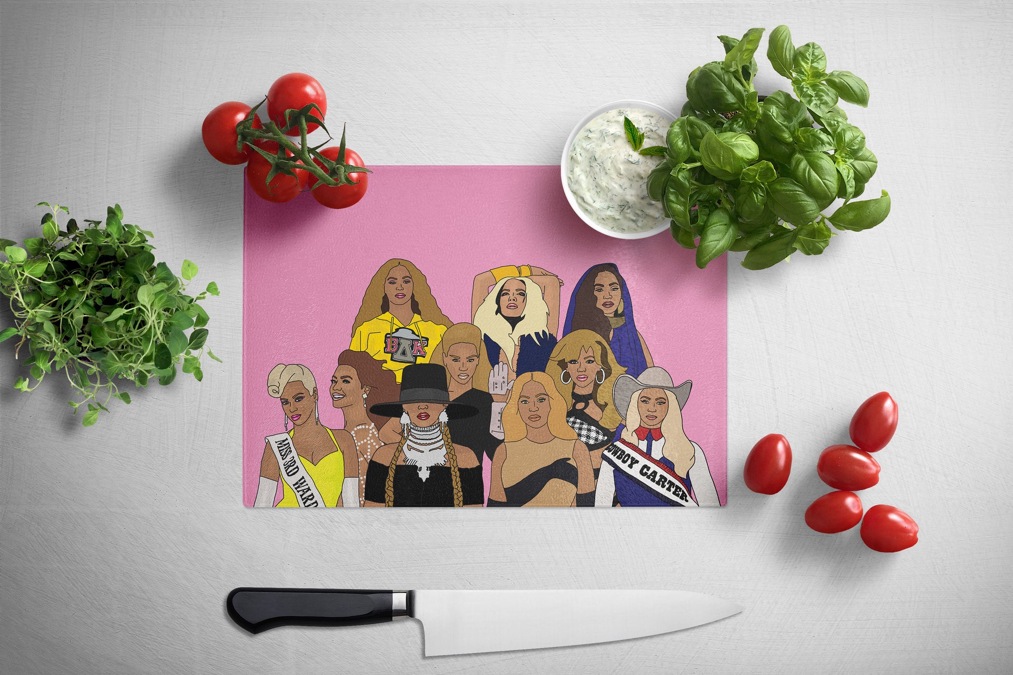 Pink cutting board with illustrated Beyonces surrounded by tomatoes and basil on a white surface
